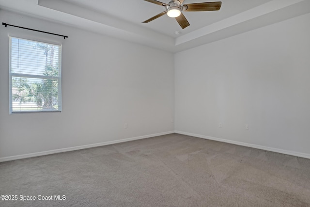 carpeted spare room with baseboards, a ceiling fan, and a tray ceiling