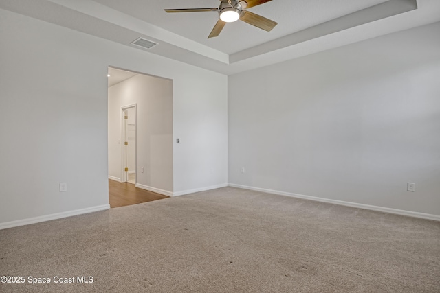 carpeted spare room with a tray ceiling, visible vents, a ceiling fan, and baseboards