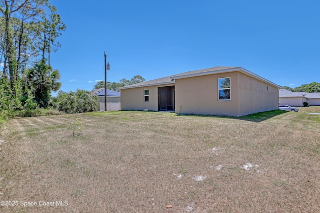 rear view of property featuring a yard and stucco siding