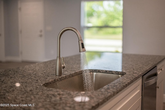 interior details featuring white cabinets, dishwasher, a sink, and dark stone countertops