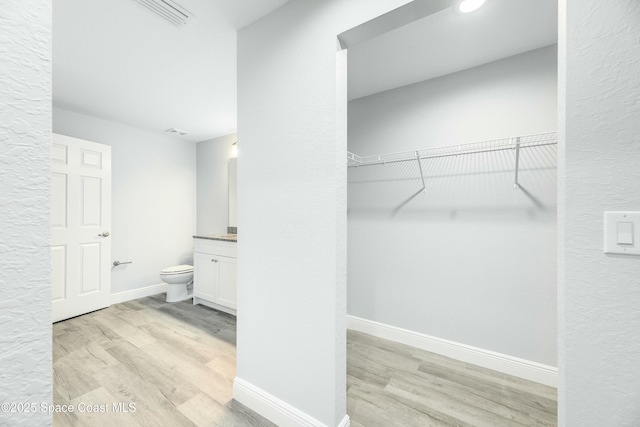 bathroom with toilet, baseboards, a spacious closet, wood finished floors, and vanity