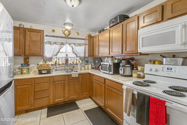 kitchen with a sink, brown cabinets, white appliances, light tile patterned floors, and light countertops