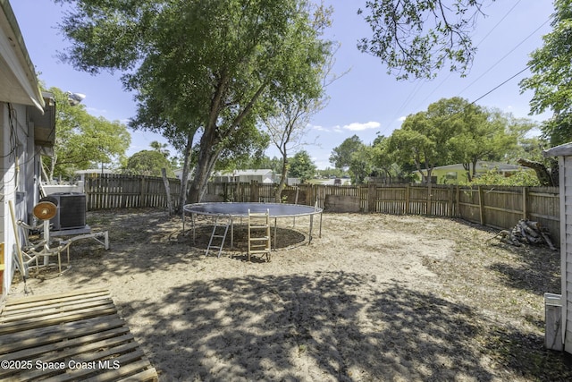 view of yard with a trampoline, a fenced backyard, and central AC unit
