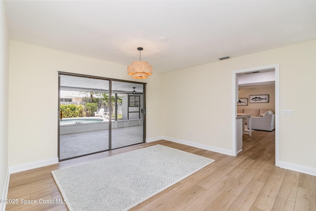 spare room with visible vents, a notable chandelier, wood finished floors, and baseboards
