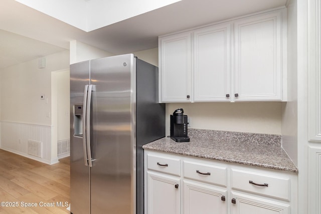 kitchen with light stone countertops, light wood-style flooring, stainless steel fridge with ice dispenser, white cabinets, and visible vents