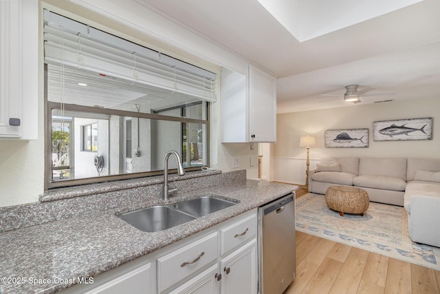 kitchen featuring light wood finished floors, a sink, dishwasher, white cabinets, and open floor plan