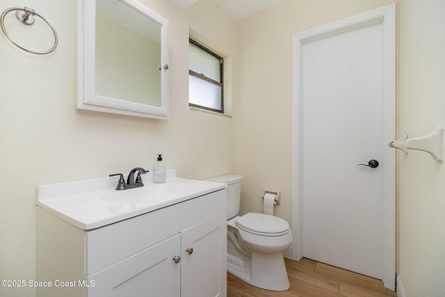 half bath featuring wood finished floors, toilet, and vanity