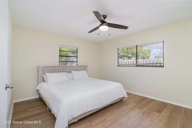 bedroom with a textured ceiling, wood finished floors, ceiling fan, and baseboards