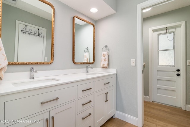 full bathroom featuring double vanity, a sink, wood finished floors, and baseboards