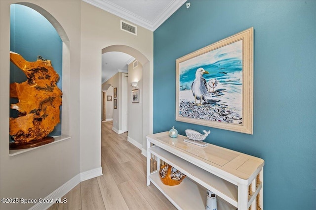 hall with arched walkways, baseboards, visible vents, wood finished floors, and crown molding