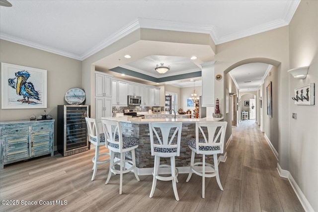 dining room with light wood-type flooring, arched walkways, beverage cooler, and ornamental molding