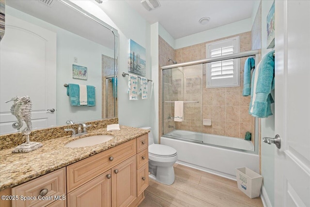 bathroom featuring bath / shower combo with glass door, toilet, visible vents, wood finished floors, and vanity