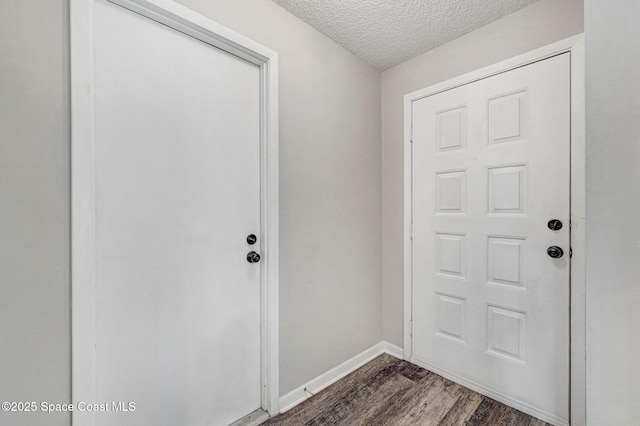 doorway with a textured ceiling, baseboards, and dark wood-type flooring
