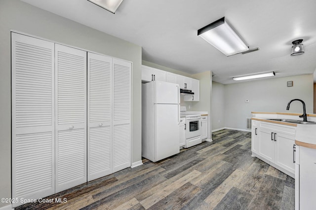 kitchen featuring white appliances, under cabinet range hood, white cabinets, a sink, and dark wood-style floors