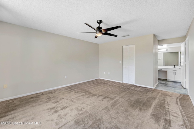 unfurnished bedroom featuring a textured ceiling, carpet flooring, visible vents, baseboards, and ensuite bath