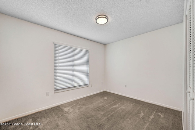 spare room with a textured ceiling, carpet flooring, and baseboards