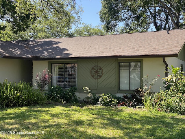 back of house with a yard, roof with shingles, and stucco siding