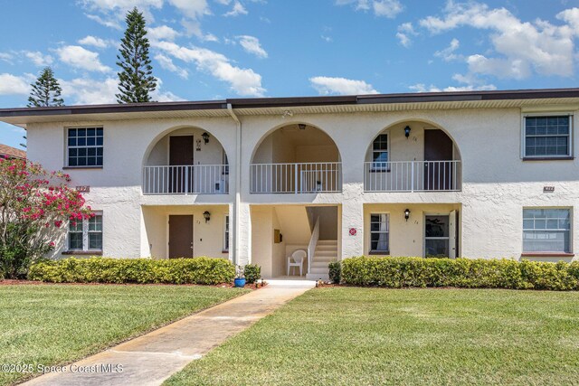 view of front of property featuring a front lawn, a balcony, and stucco siding