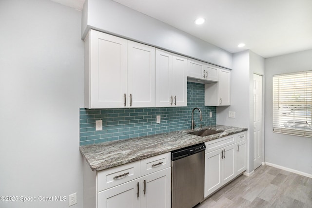 kitchen with stainless steel dishwasher, tasteful backsplash, a sink, and light wood-style floors