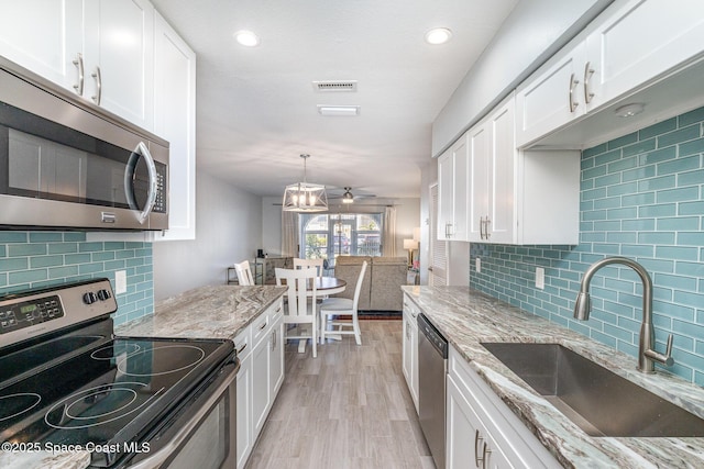 kitchen featuring stainless steel appliances, a sink, light wood-style floors, white cabinetry, and light stone counters