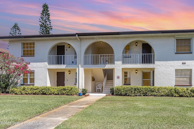 view of front facade featuring stucco siding, a front lawn, and a balcony