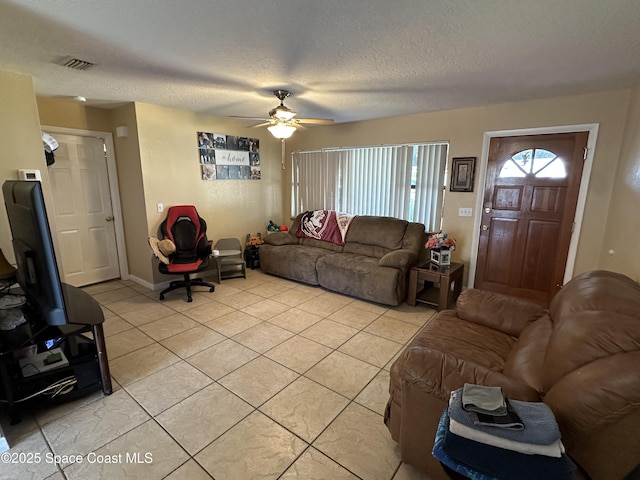 living area featuring visible vents, a ceiling fan, light tile patterned floors, baseboards, and a textured ceiling