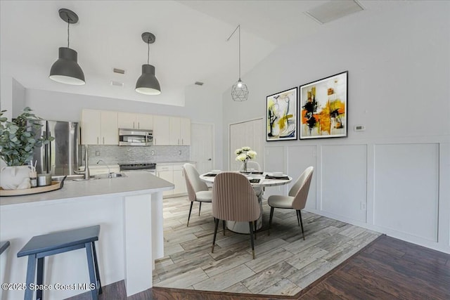 194 Saybrook Rd SW, Palm Bay, FL 32908 - dining space featuring wainscoting, high vaulted ceiling, a decorative wall, and light wood-style flooring