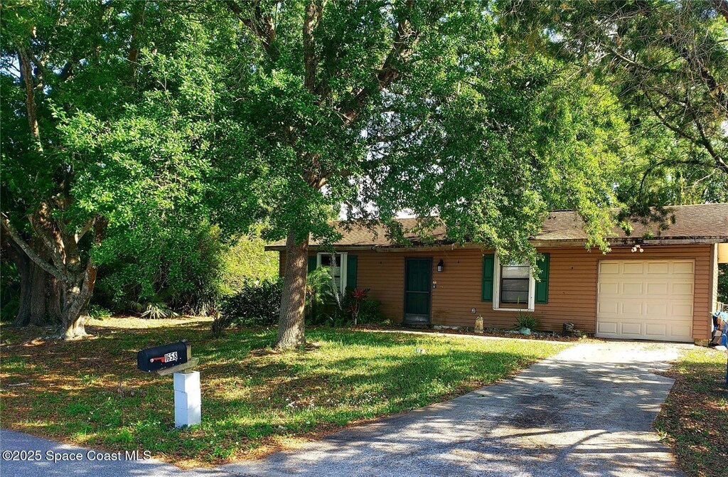 single story home with concrete driveway, an attached garage, and a front lawn