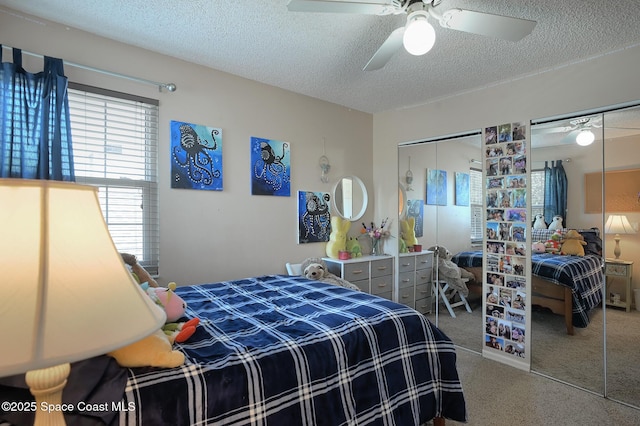carpeted bedroom with two closets, a ceiling fan, multiple windows, and a textured ceiling