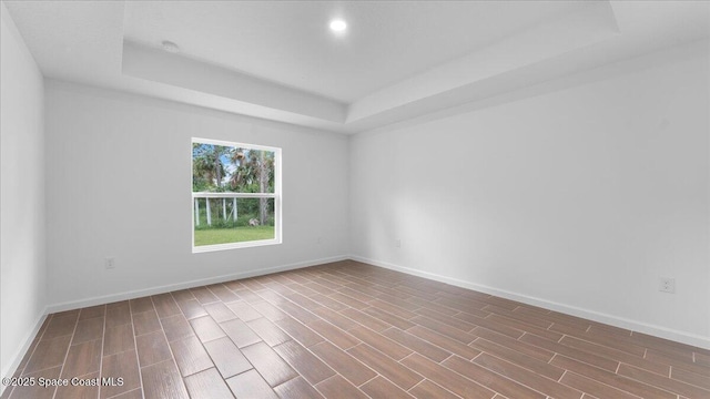 empty room with baseboards, wood finished floors, and a tray ceiling