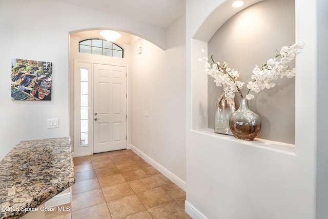 foyer with baseboards, arched walkways, and light tile patterned floors
