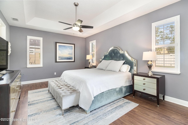 bedroom with a ceiling fan, wood finished floors, a tray ceiling, baseboards, and visible vents