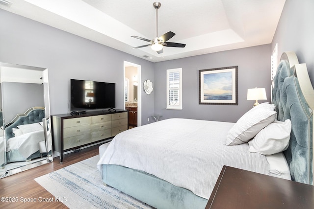 bedroom featuring ceiling fan, a tray ceiling, wood finished floors, and ensuite bathroom