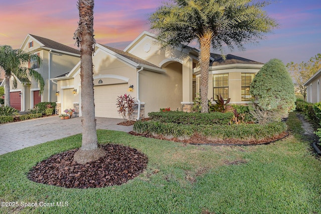 mediterranean / spanish house with stucco siding, an attached garage, decorative driveway, and a front yard