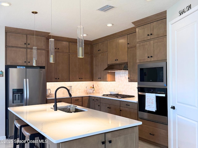 kitchen with under cabinet range hood, stainless steel appliances, backsplash, visible vents, and a sink