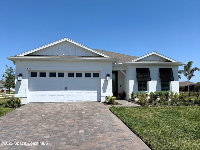 view of front of home with decorative driveway, a garage, board and batten siding, a front yard, and stucco siding