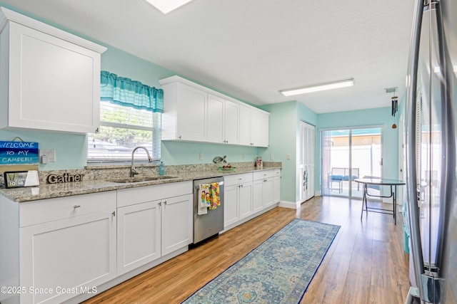 kitchen featuring white cabinets, stainless steel appliances, a sink, light wood-type flooring, and light stone countertops