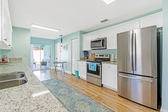 kitchen with light wood finished floors, white cabinets, visible vents, light stone countertops, and appliances with stainless steel finishes