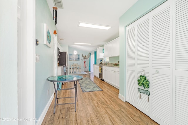 corridor with light wood finished floors, a sink, baseboards, visible vents, and lofted ceiling