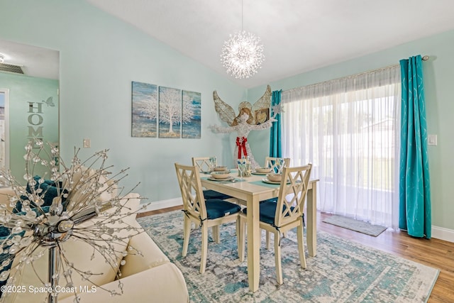 dining space with an inviting chandelier, vaulted ceiling, wood finished floors, visible vents, and baseboards
