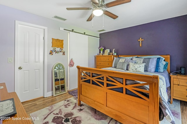 bedroom with a barn door, a ceiling fan, wood finished floors, and visible vents