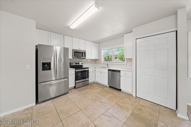 kitchen with stainless steel appliances, light countertops, white cabinetry, decorative backsplash, and a sink