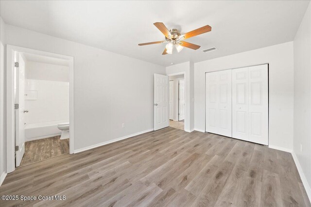 unfurnished bedroom featuring wood finished floors, a closet, baseboards, connected bathroom, and a ceiling fan