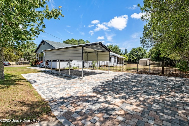 view of parking featuring decorative driveway, a detached carport, and fence