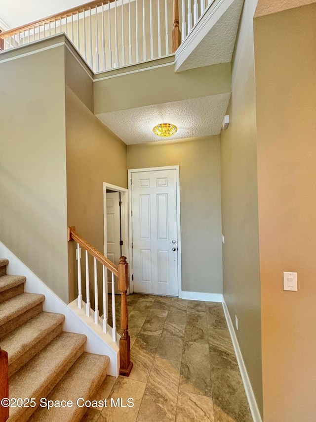 foyer with baseboards, stone finish floor, and stairs