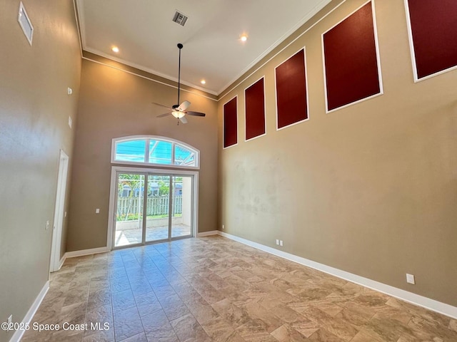 empty room featuring a ceiling fan, a high ceiling, baseboards, ornamental molding, and visible vents