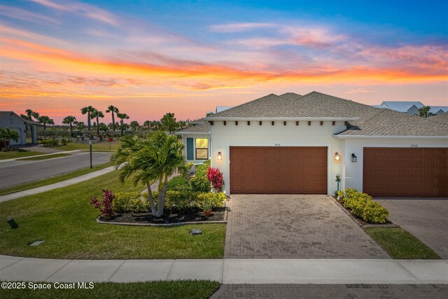 view of front of property with stucco siding, decorative driveway, a lawn, and an attached garage