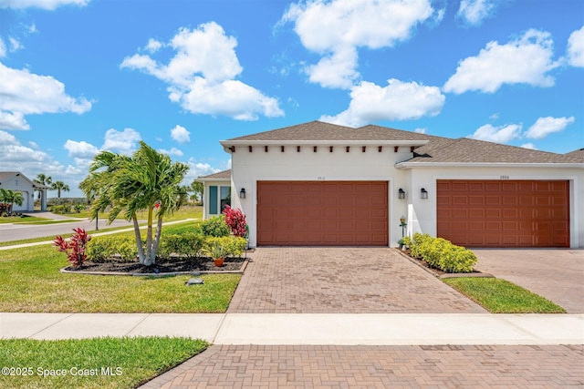 view of front of house featuring a front yard, stucco siding, decorative driveway, and an attached garage
