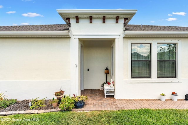 doorway to property with stucco siding and roof with shingles