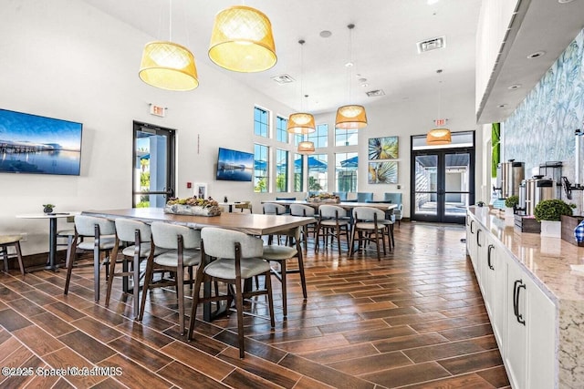dining space featuring a healthy amount of sunlight, visible vents, wood tiled floor, and a high ceiling
